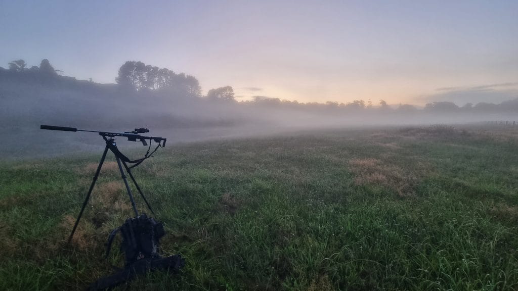 Rifle on tripod in a paddock, fog all around, turning things in the distance fading to white
